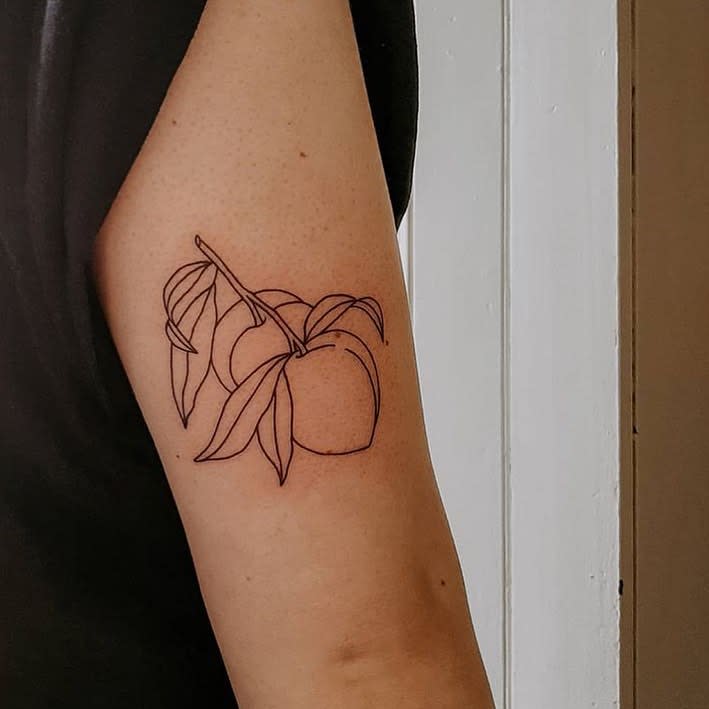 Outline tattoo of two peaches with leaves on an upper arm
